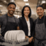 Hotel kitchen steward holding a rack of clean plates with a manager and chef in a clean commercial kitchen.